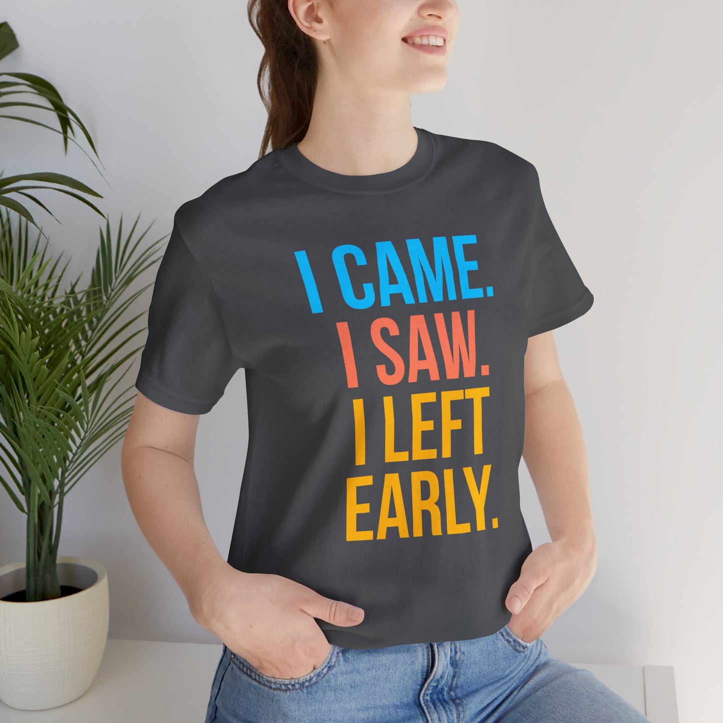 Person wearing a black t-shirt with colorful text 'I CAME. I SAW. I LEFT EARLY.' in a room with a plant.