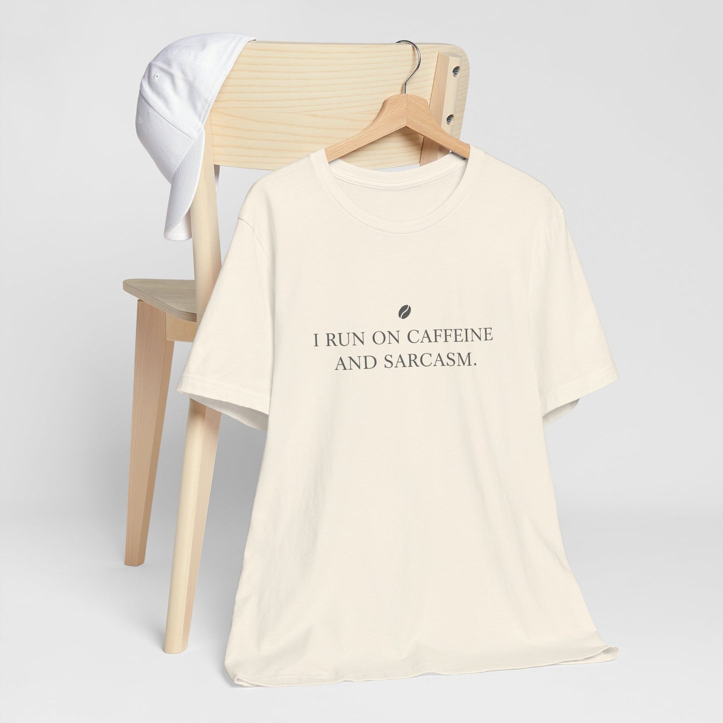 Beige t-shirt with text 'I run on caffeine and sarcasm' on a chair against a white background