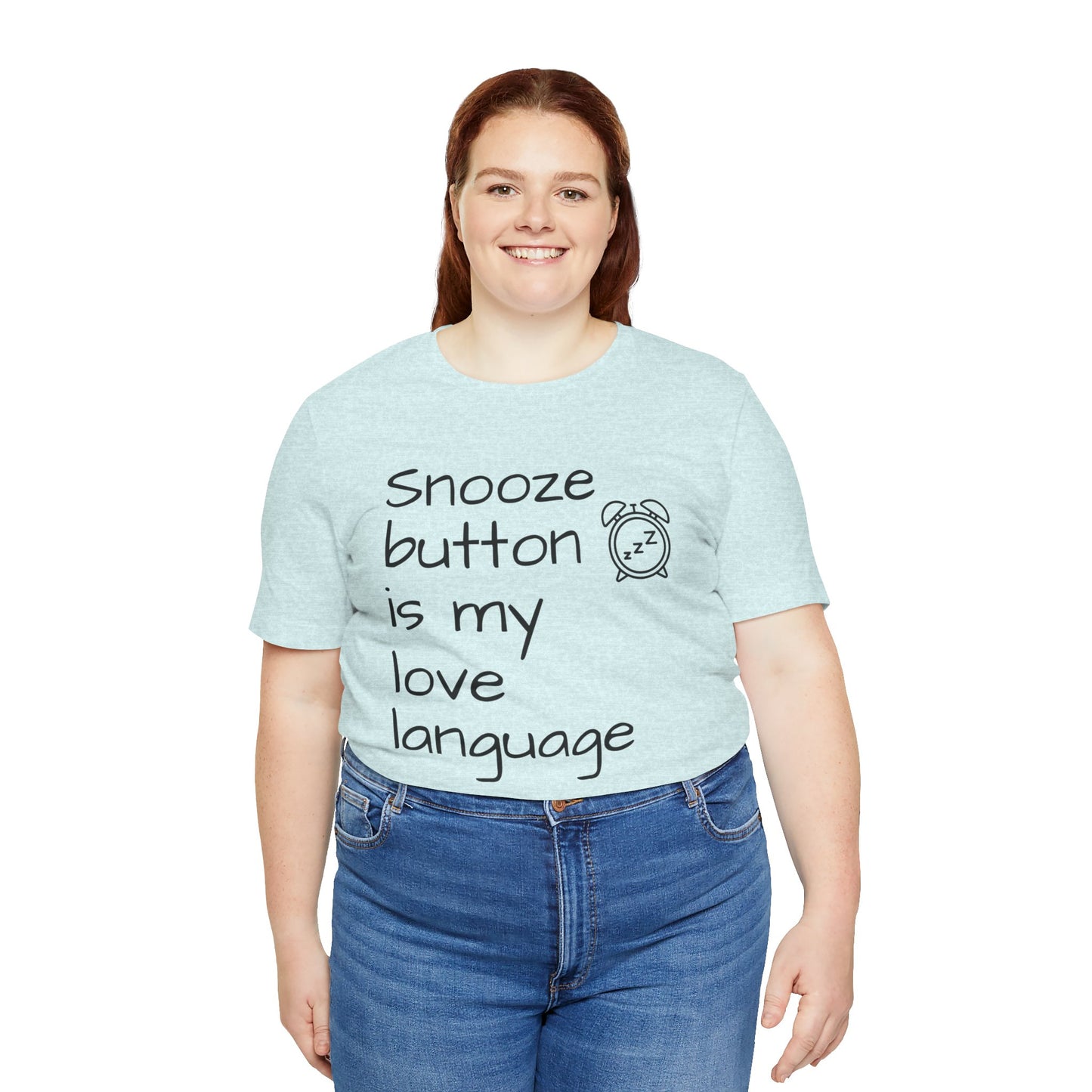 Person wearing a light blue t-shirt with text 'Snooze button is my love language' and jeans on a white background