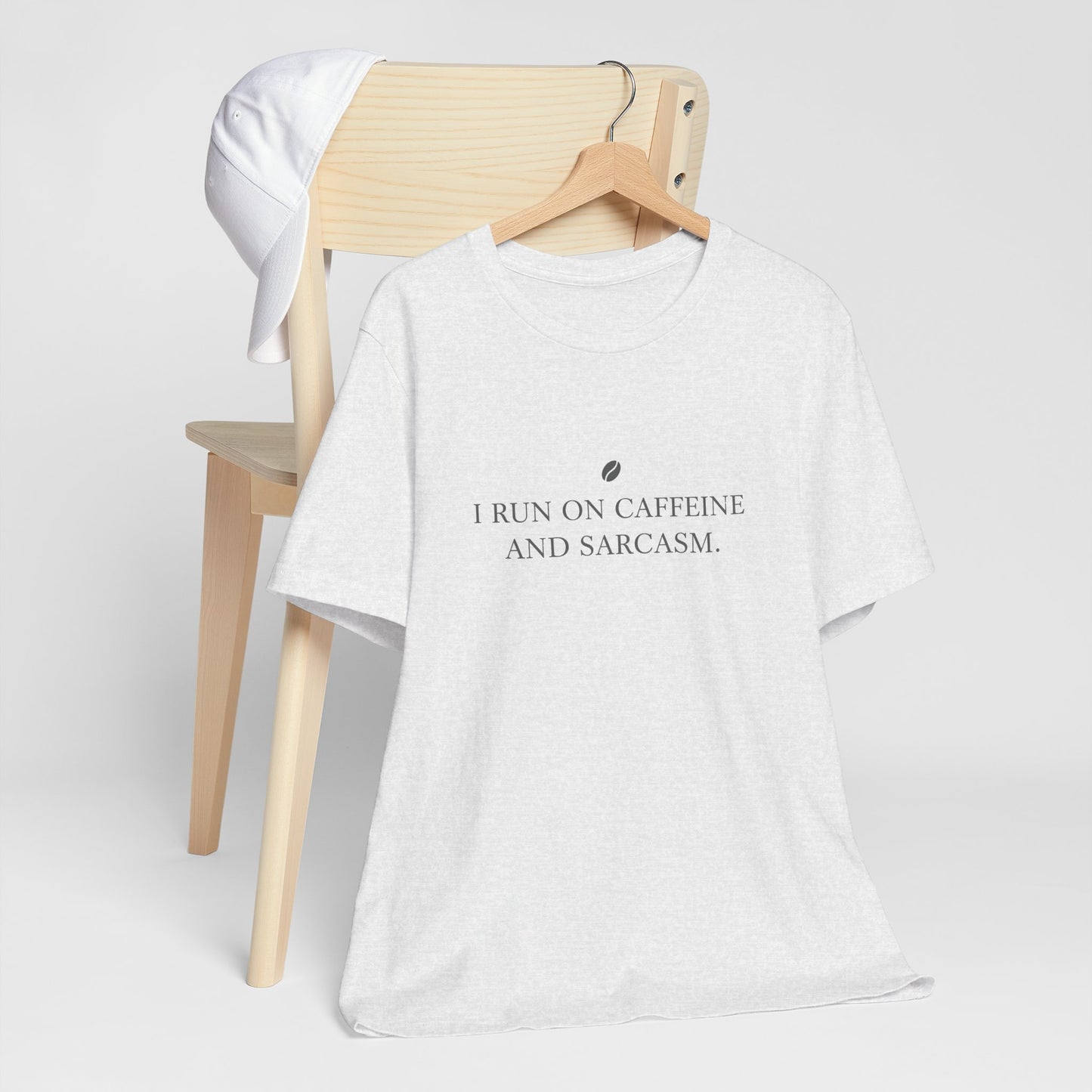 White t-shirt with text 'I run on caffeine and sarcasm' on a wooden chair.