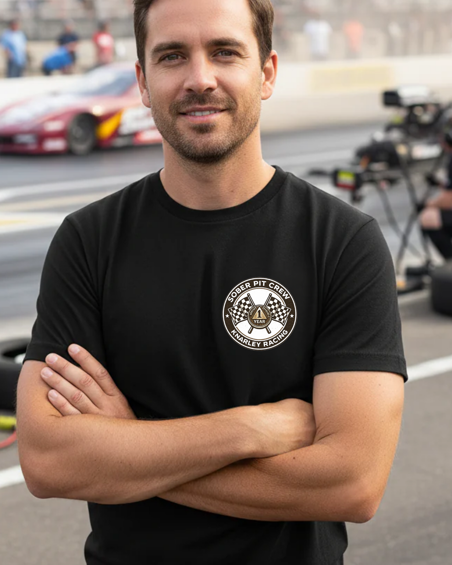 Man wearing a black t-shirt with a 'Sober Pit Crew Knarley Racing' logo on a race track