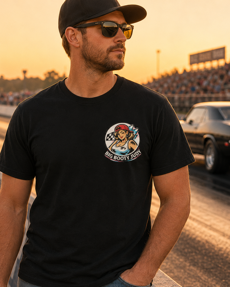 Man wearing a black t-shirt with a Big Booty Judy logo graphic design on a race track at sunset