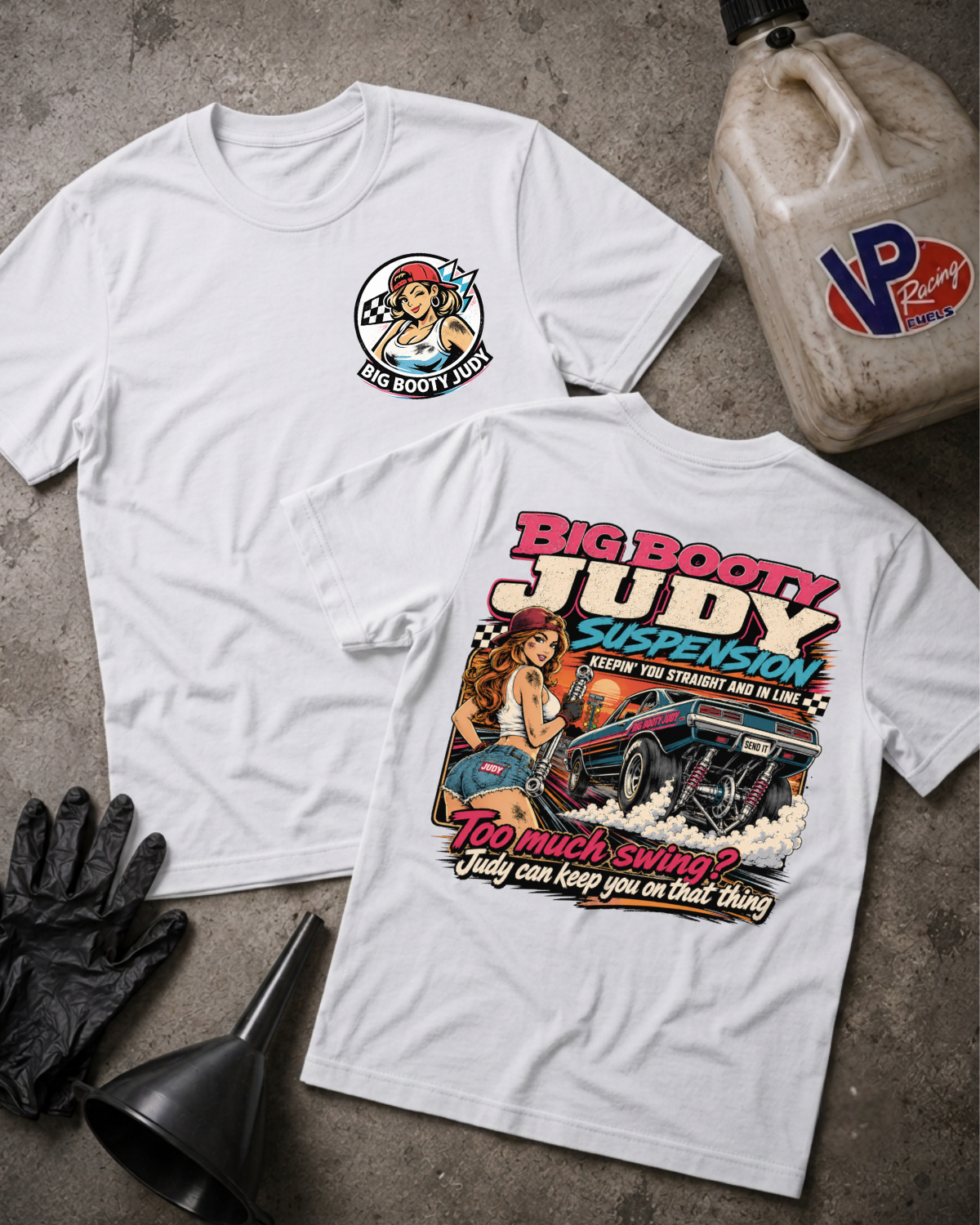 Two white graphic T-shirts laid flat on a gray concrete surface, with a large vintage-style front print and a smaller circular chest print on the front shirt, plus a large VP Racing jug, black gloves, and a funnel as props.