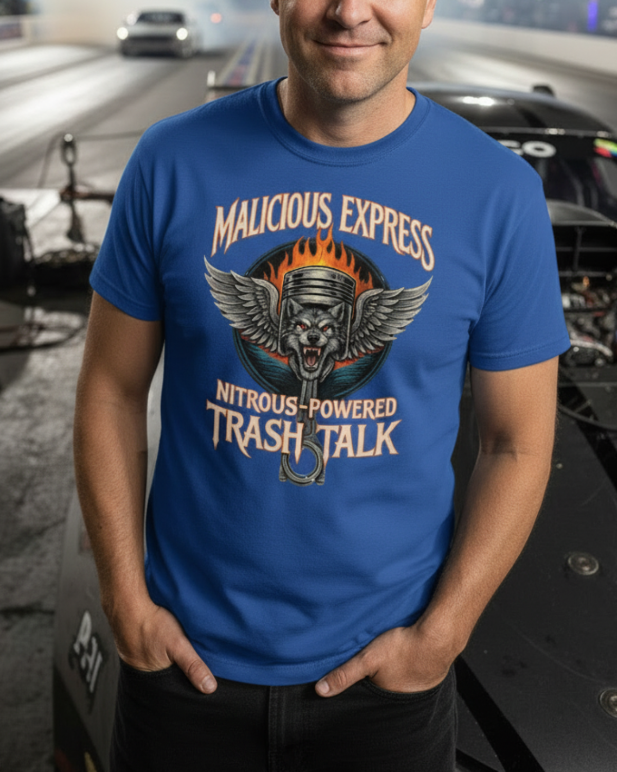Man wearing a blue t-shirt with graphic design and 'Malicious Express Nitrous-Powered Trash Talk' text, standing on a racetrack with cars and smoke in the background.