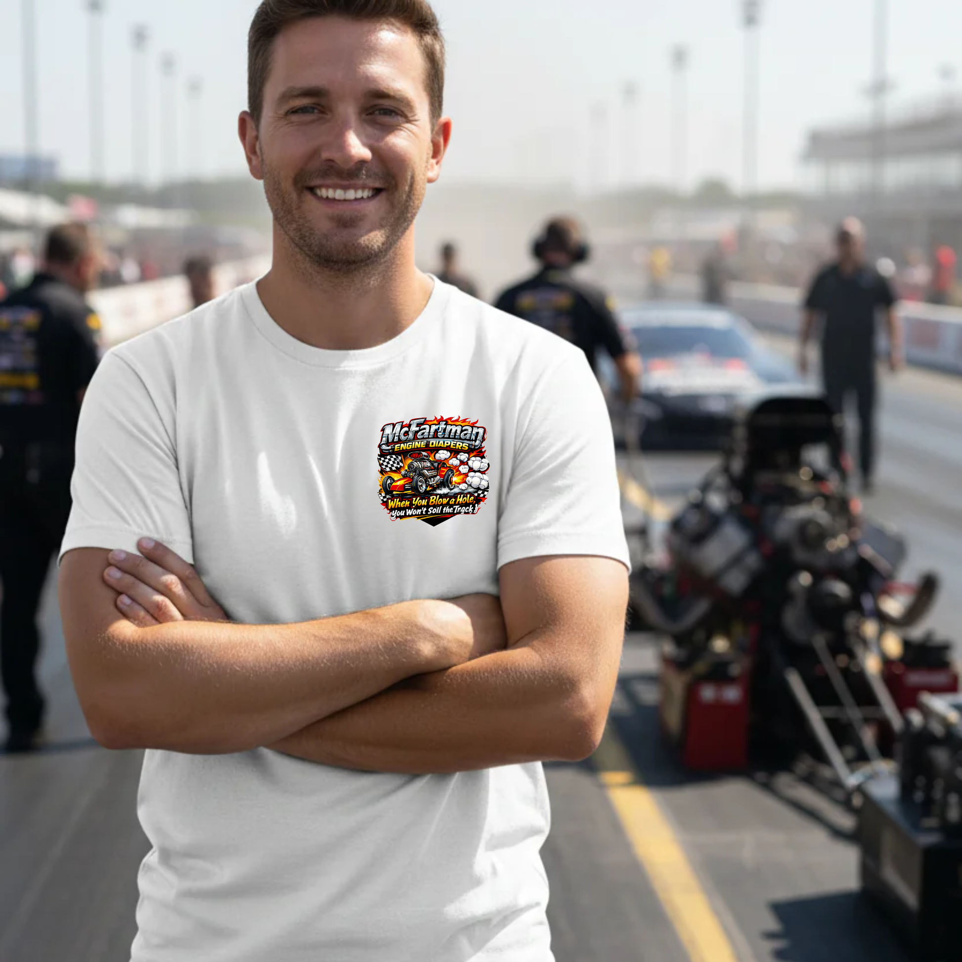 Man wearing a white t-shirt with a colorful graphic design 'McFartman Engine Diapers' logo on a race track.