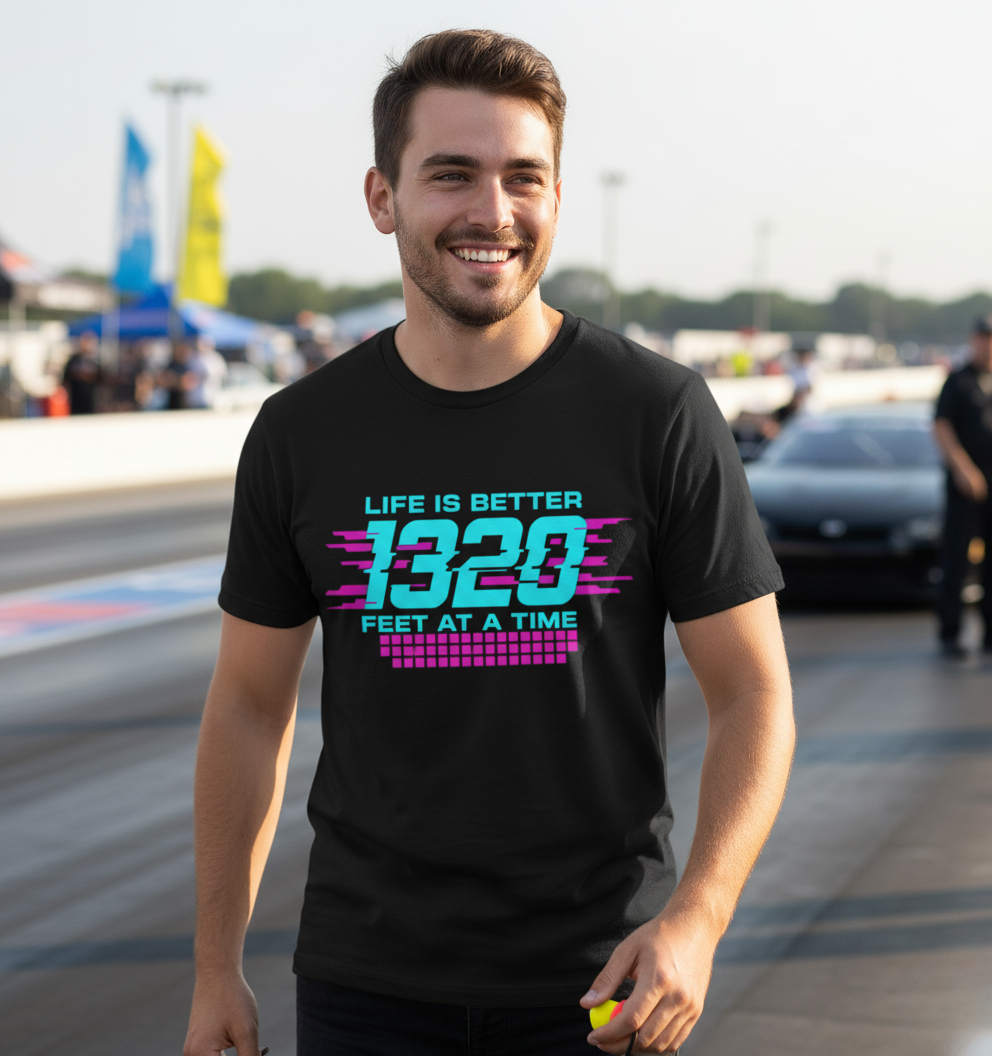 Man wearing a black t-shirt with a colorful graphic and text 'Life is better 1320 feet at a time' at a race track.