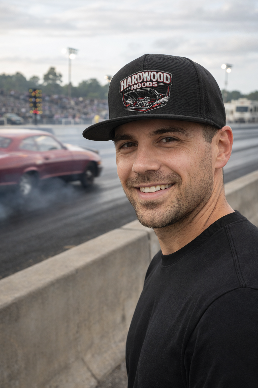 Man wearing a cap with 'Hardwood Hoods' logo at a drag racing event
