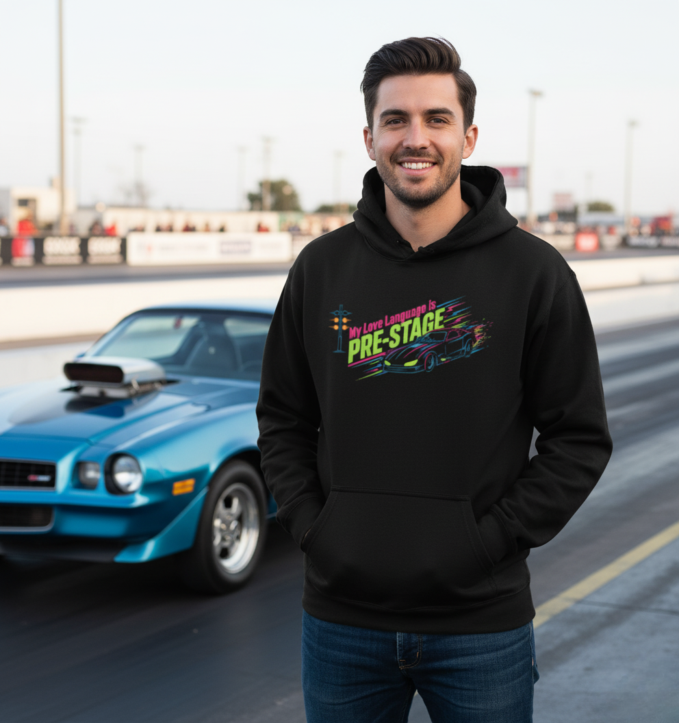 Man wearing a black hoodie with colorful text 'My Love Language is Pre-Stage' in front of a blue car on a track