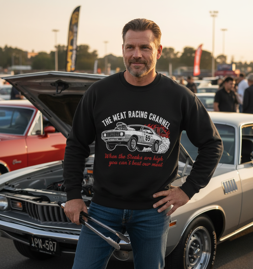 Man wearing The Meat Racing Channel sweatshirt, holding tongs while standing next to a classic silver muscle car at a car meet.