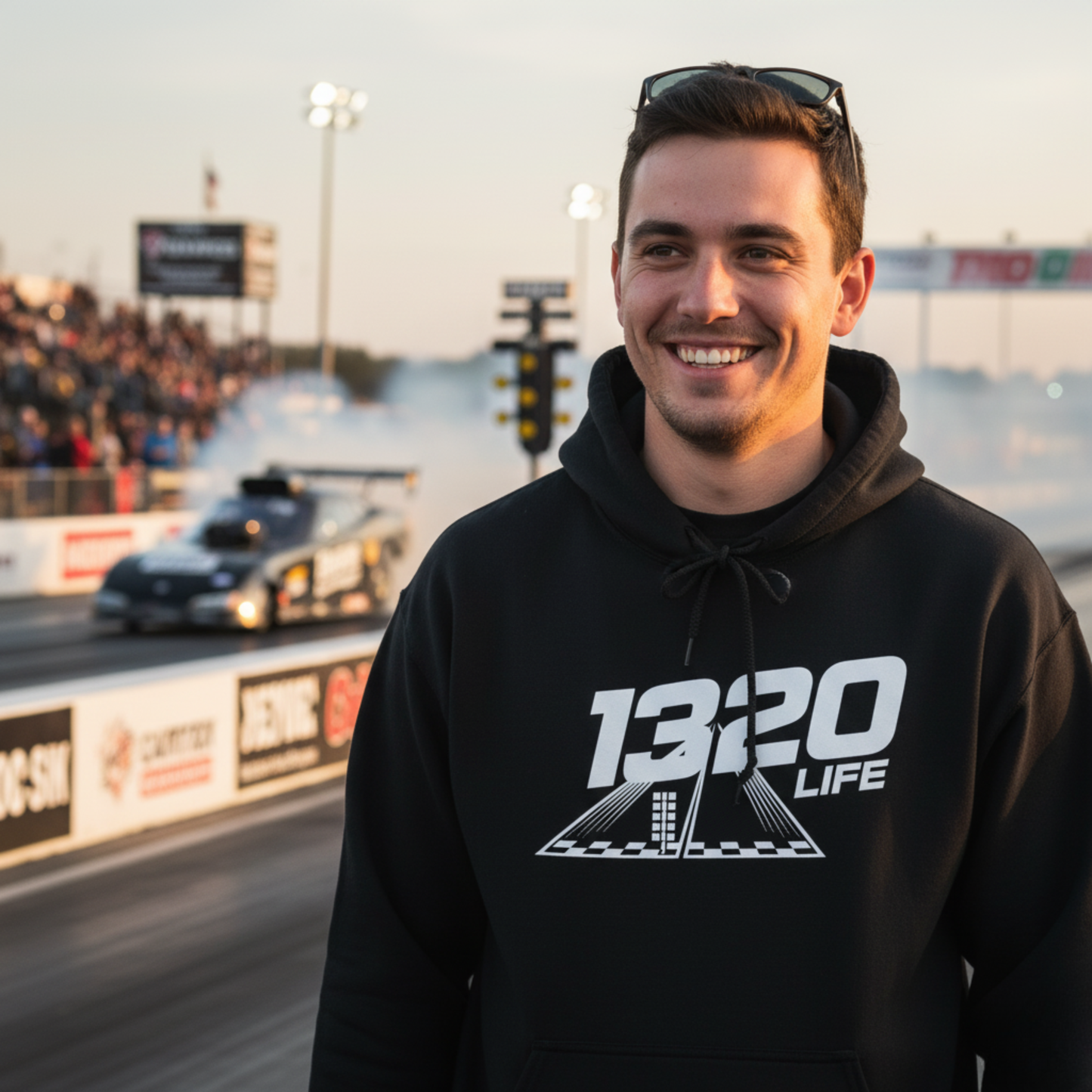 Man wearing a black hoodie with '1320 LIFE' at a race track.