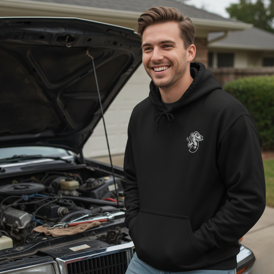 Person wearing black Gildan 18500 hoodie with white cartoon weasel chest graphic, standing beside classic car with hood open in garage setting. Ideal for drag racing fans and motorsport lifestyle."


