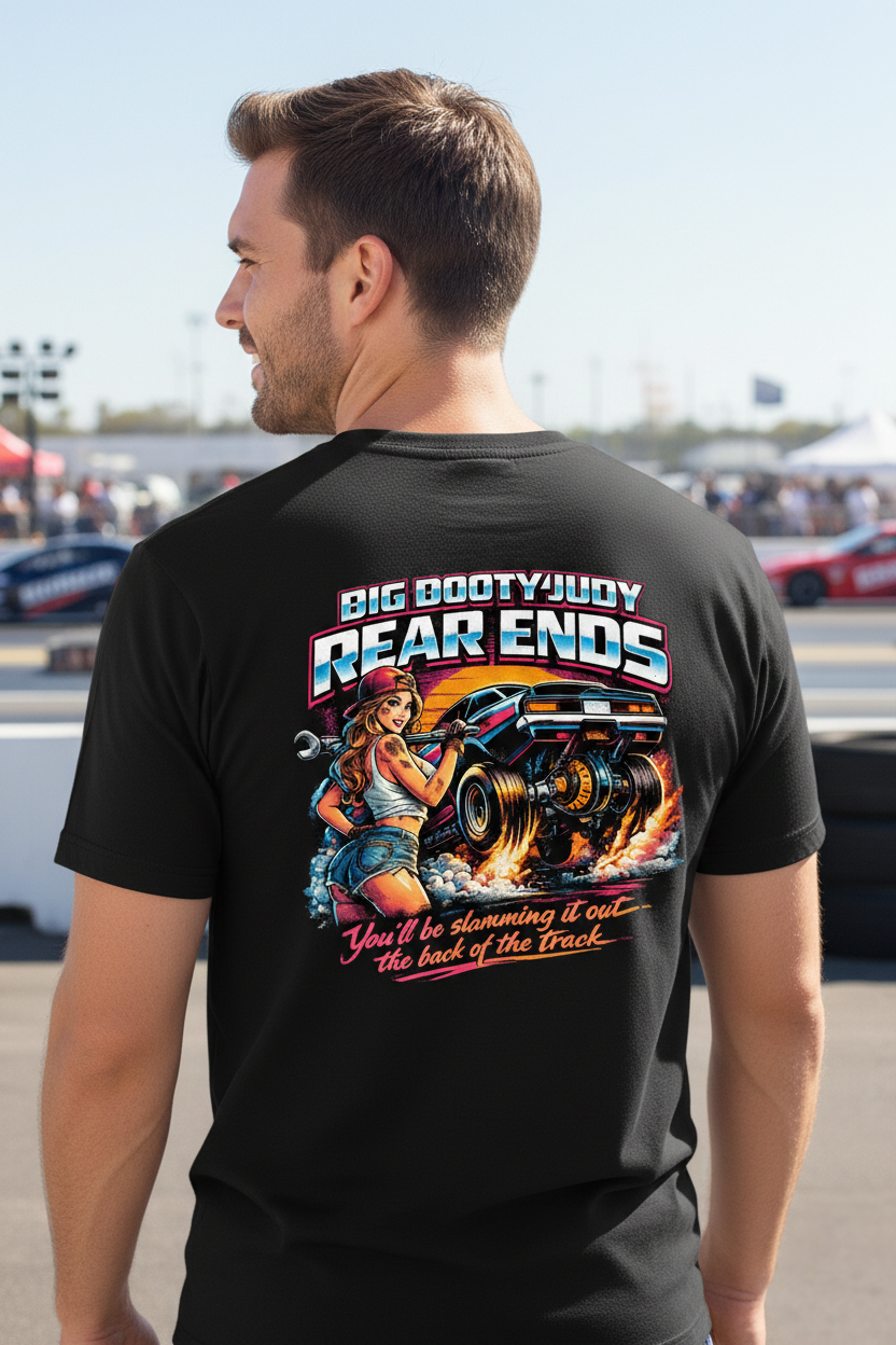 Man wearing a black t-shirt with a graphic design of a woman and a car, text 'Big Booty Juicy Rear Ends' at an outdoor event.