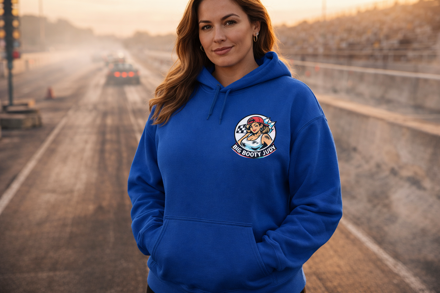 Woman wearing a blue hoodie with a 'Big Booty Judy' logo on a race track