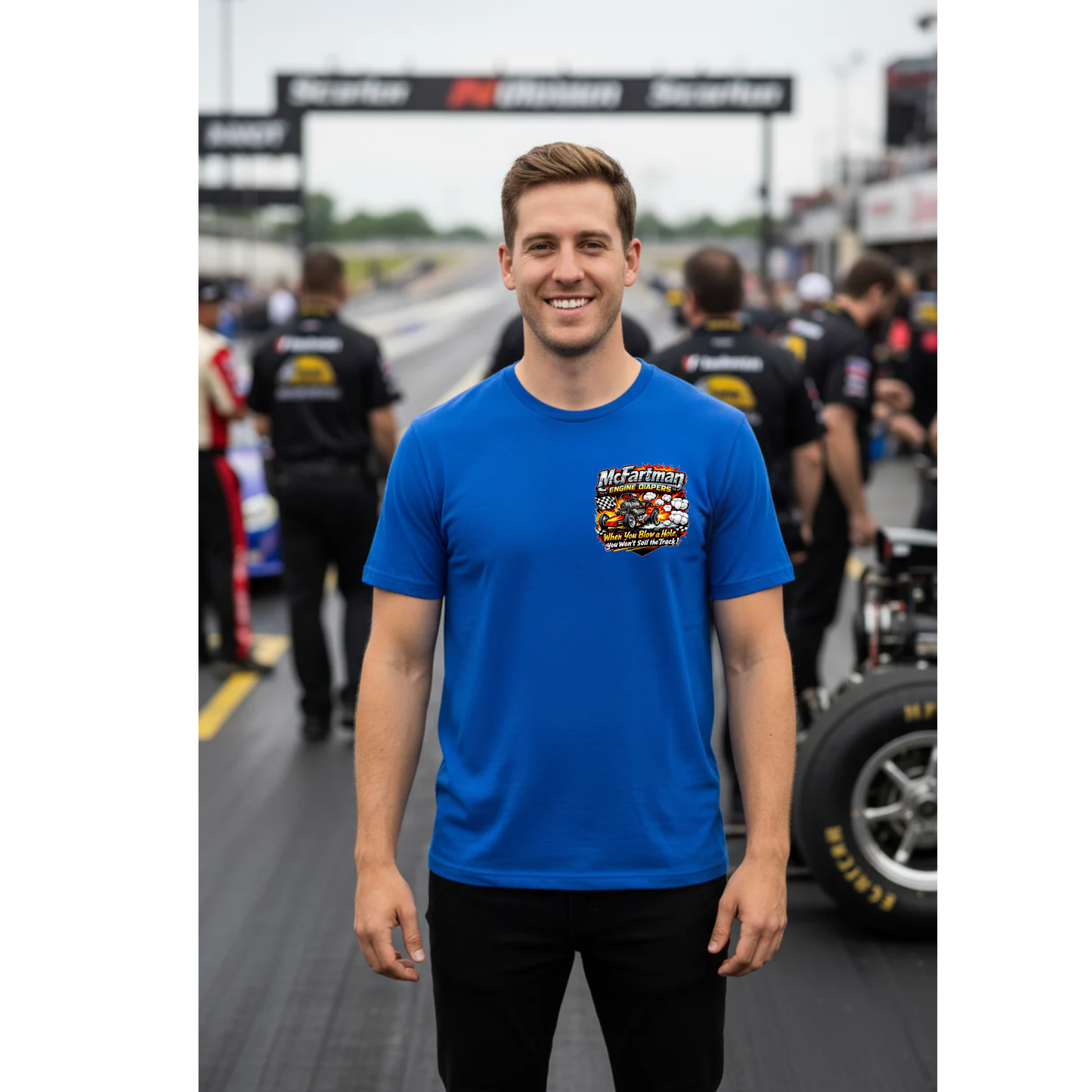 Man wearing a blue t-shirt with a 'McFartman Engine Diapers' logo on a race track