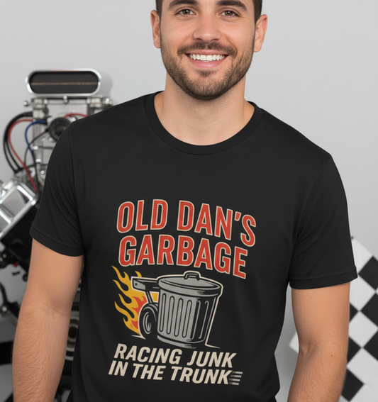 Person wearing a black graphic T‑shirt featuring the bold red and white text “Old Dan’s Garbage” above a flaming garbage can illustration, with the tagline “Racing Junk in the Trunk” below. Funny drag racing parody shirt with retro racing flames, checkered flag background, and humor‑driven hot rod style, perfect for car enthusiasts and gearhead apparel fans.
