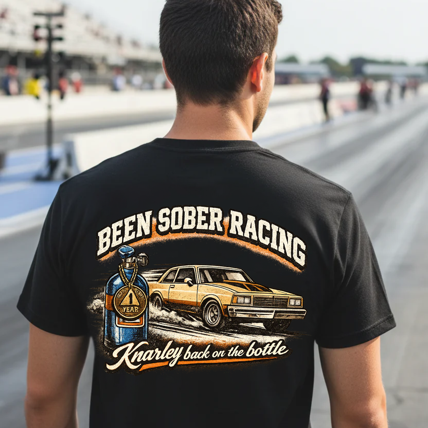 Person wearing a black t-shirt with 'Been Sober Racing' graphic at a race track.