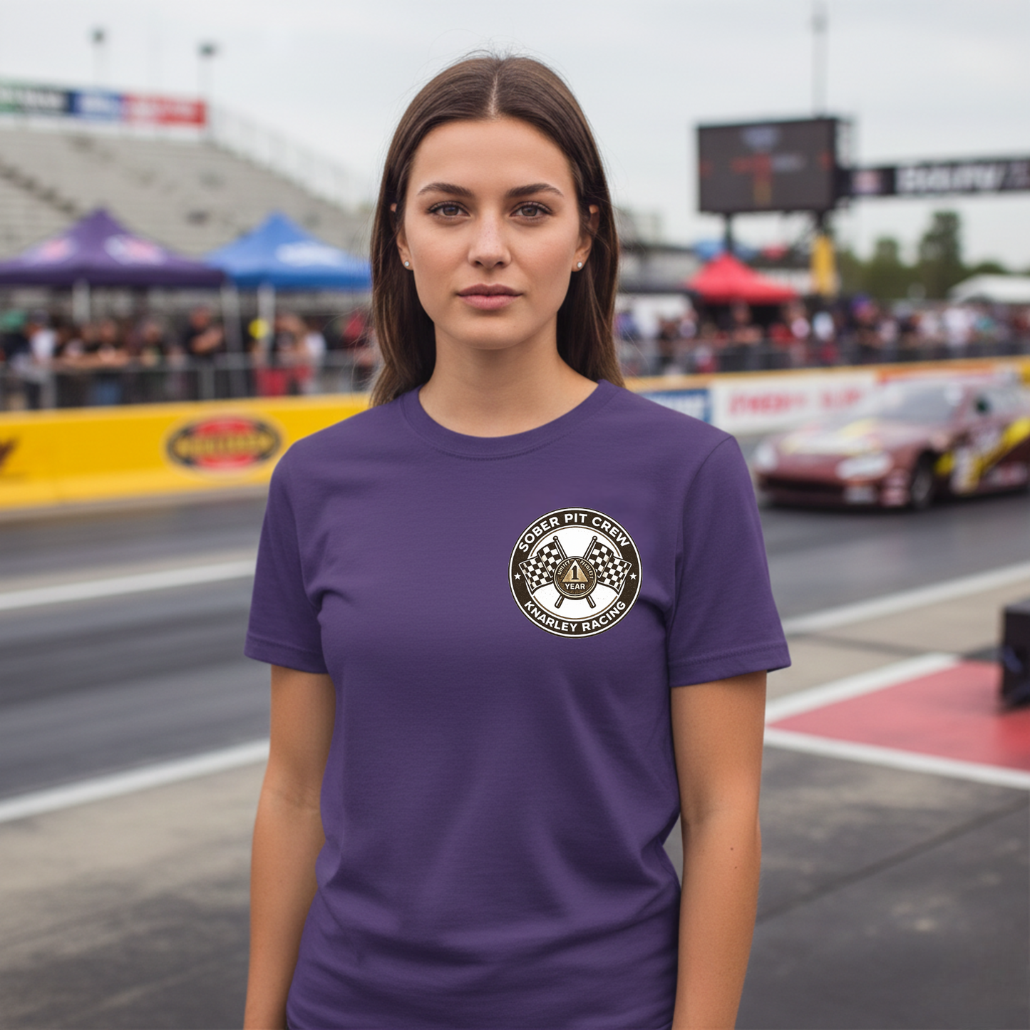 Woman wearing a purple t-shirt with a 'Sober Pit Crew Knarley Racing' logo on a race track background