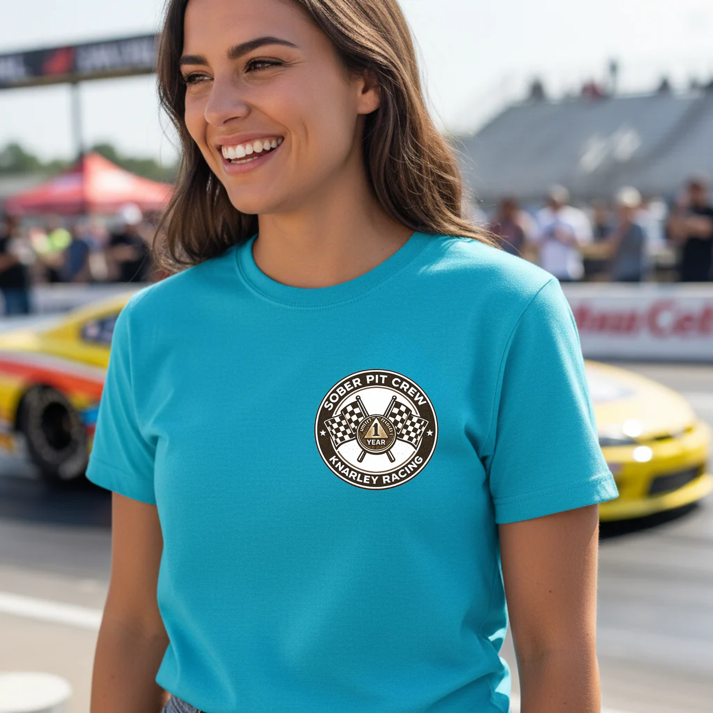 Woman wearing a aqua blue t-shirt with a 'Sober Pit Crew Knarley Racing' logo at a race track