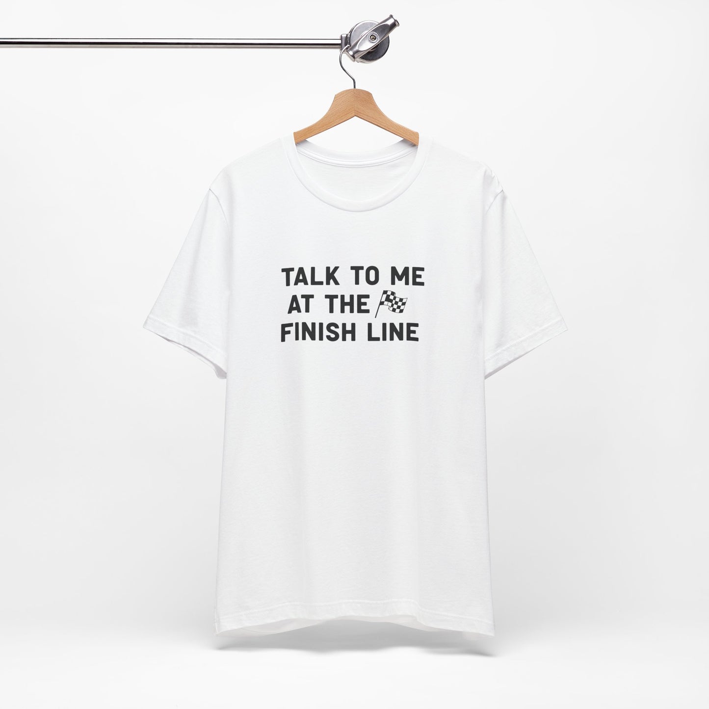 White t-shirt with text 'Talk to me at the finish line' on a hanger against a white background