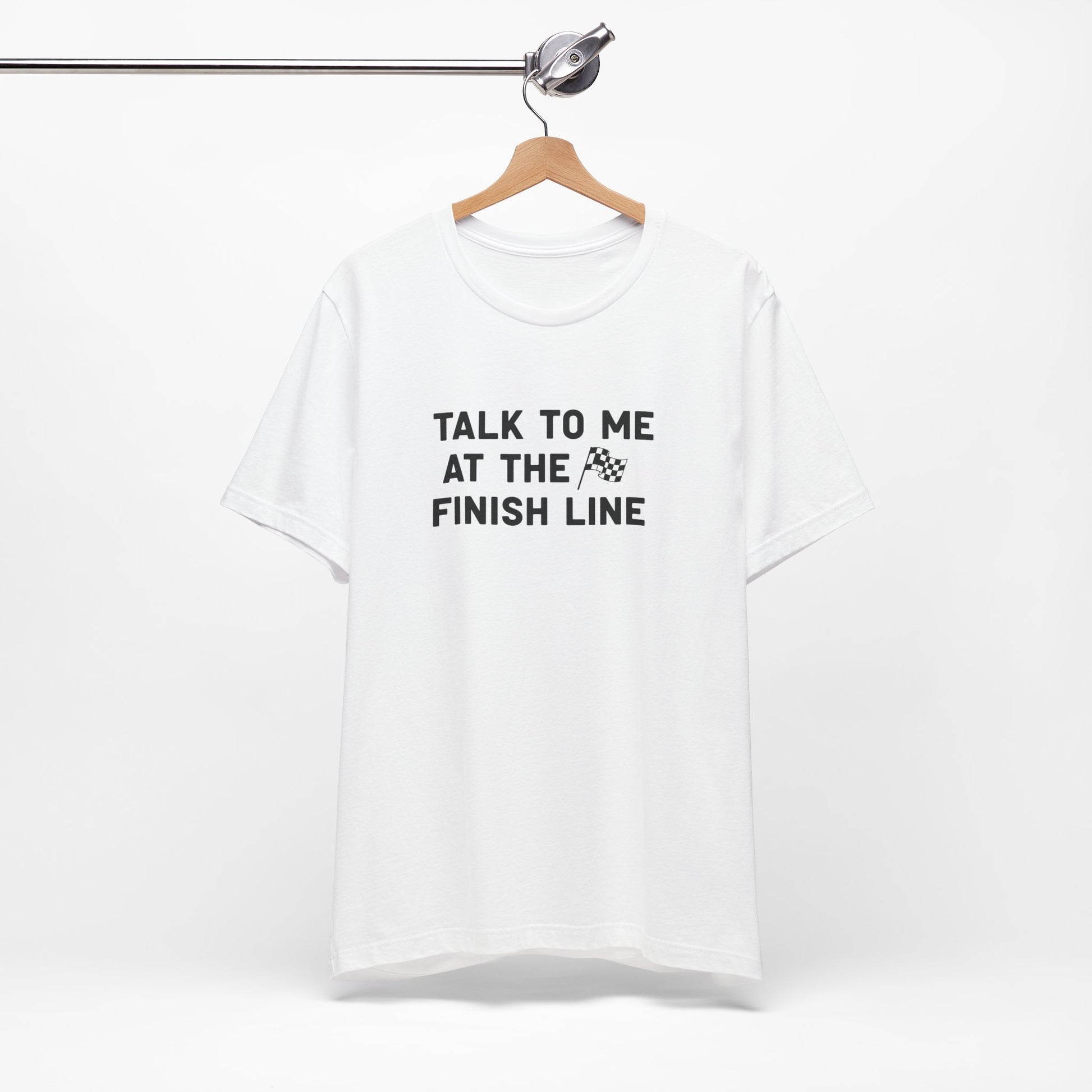 White t-shirt with text 'Talk to me at the finish line' on a hanger against a white background