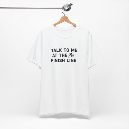 White t-shirt with text 'Talk to me at the finish line' on a hanger against a white background