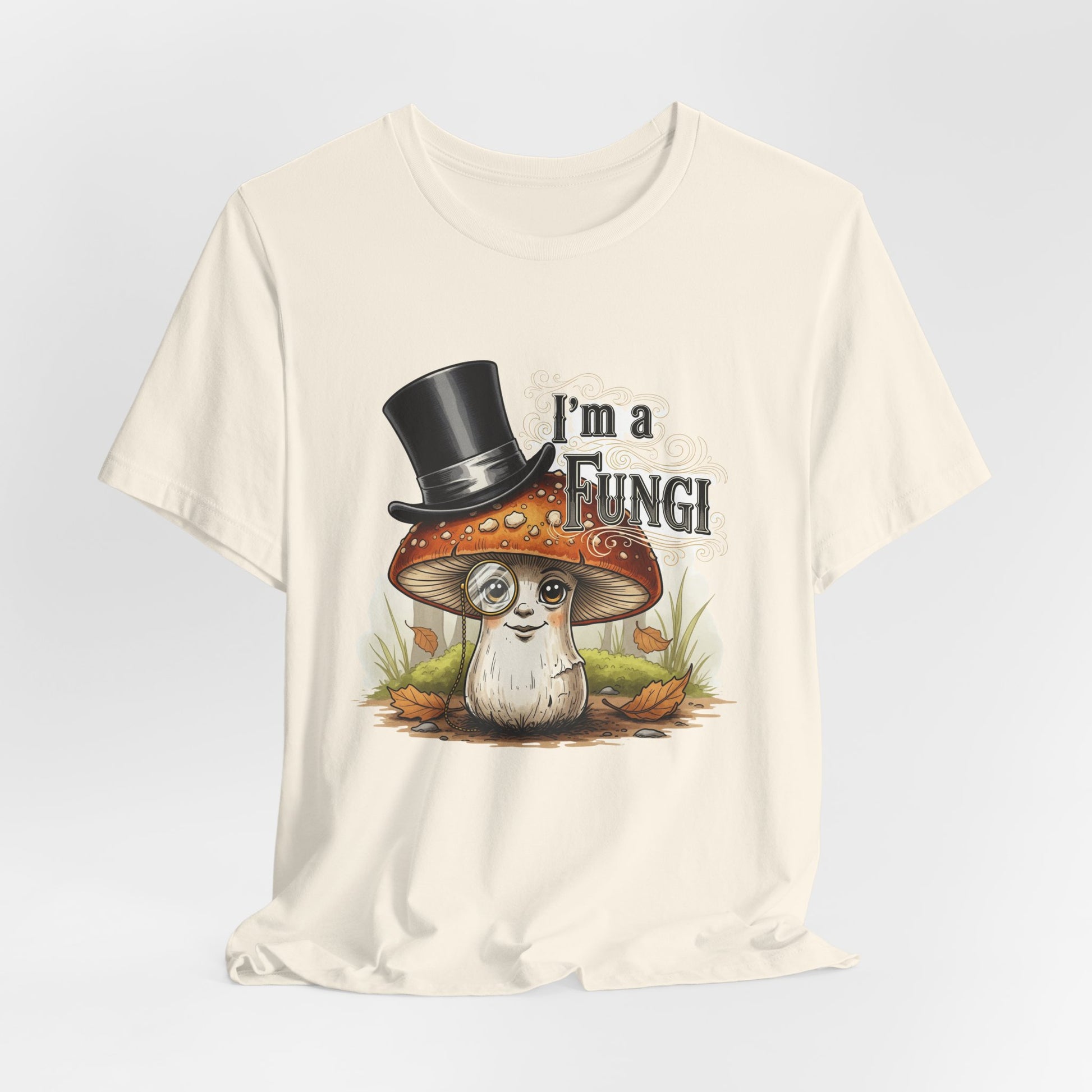 Unisex Bella+Canvas 3001 t-shirt in Natural with a quirky cartoon mushroom wearing a black top hat and monocle, surrounded by autumn leaves and grass, with bold text above reading “I’m a Fungi.”