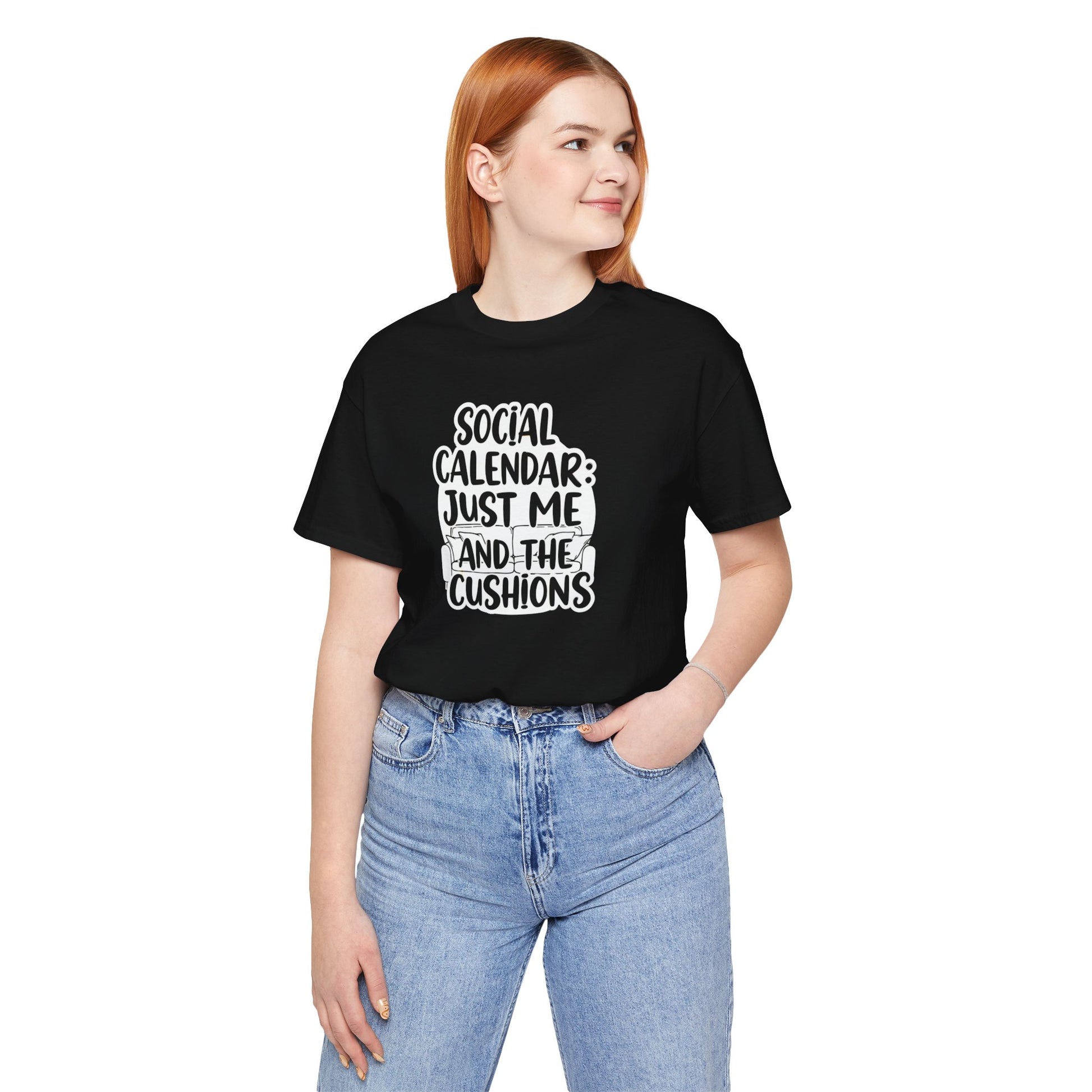Person wearing a black t-shirt with text 'Social calendar: Just me and the cushions', standing against a white background