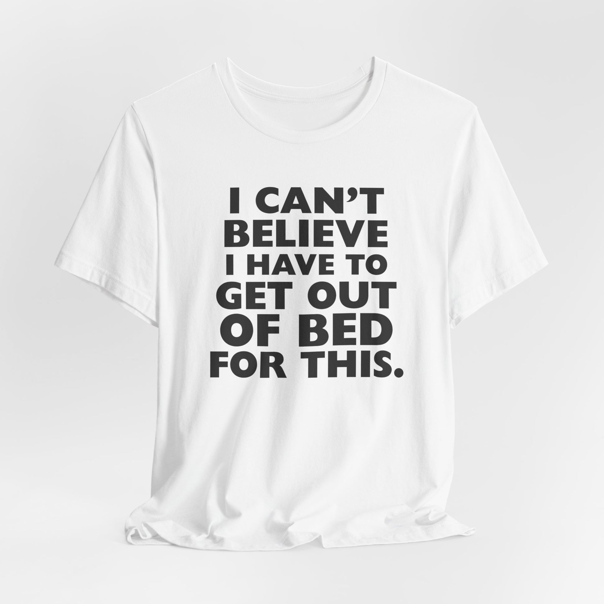 White t-shirt with black text 'I can't believe I have to get out of bed for this' on a white background