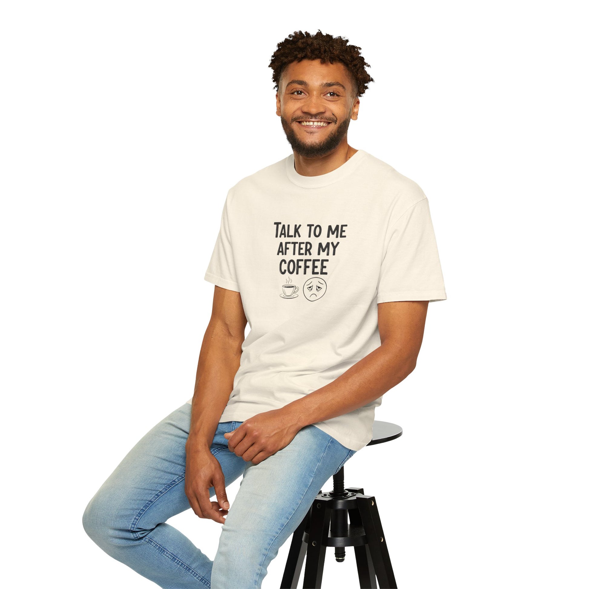 Man sitting on a stool wearing a white t-shirt with text 'Talk to me after my coffee' and jeans on a white background