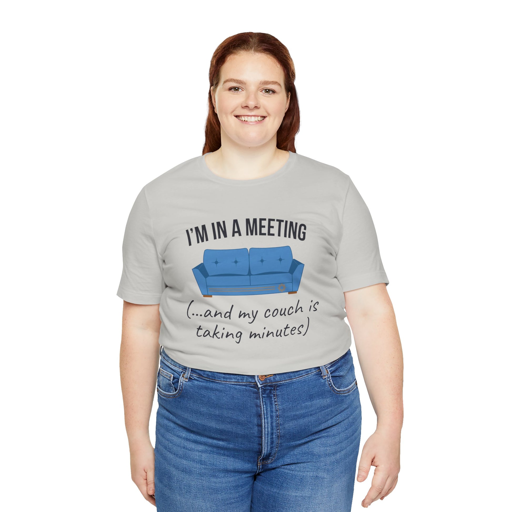 Person wearing a gray t-shirt with a humorous graphic and text 'I'm in a meeting (...and my couch is taking minutes)'on a white background