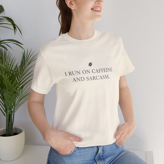 Person wearing a white t-shirt with text 'I run on caffeine and sarcasm', standing next to a plant against a light background