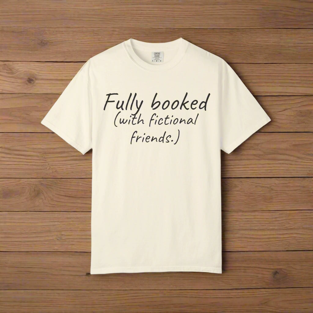 Beige t-shirt with text 'Fully booked (with fictional friends.)' on a wooden background