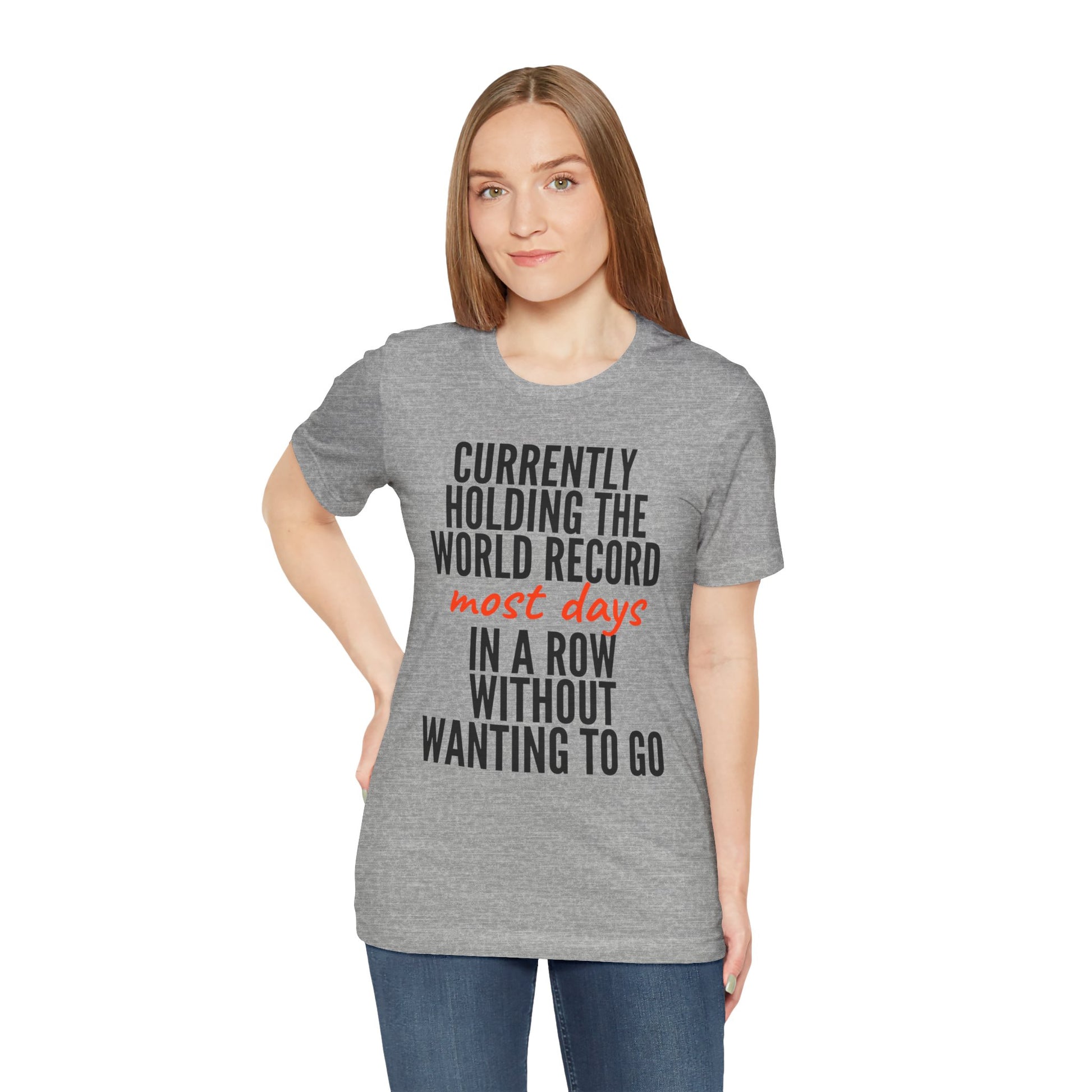 Woman wearing a gray t-shirt with humorous text 'Currently holding the world record most days in a row without wanting to go' design on a white background