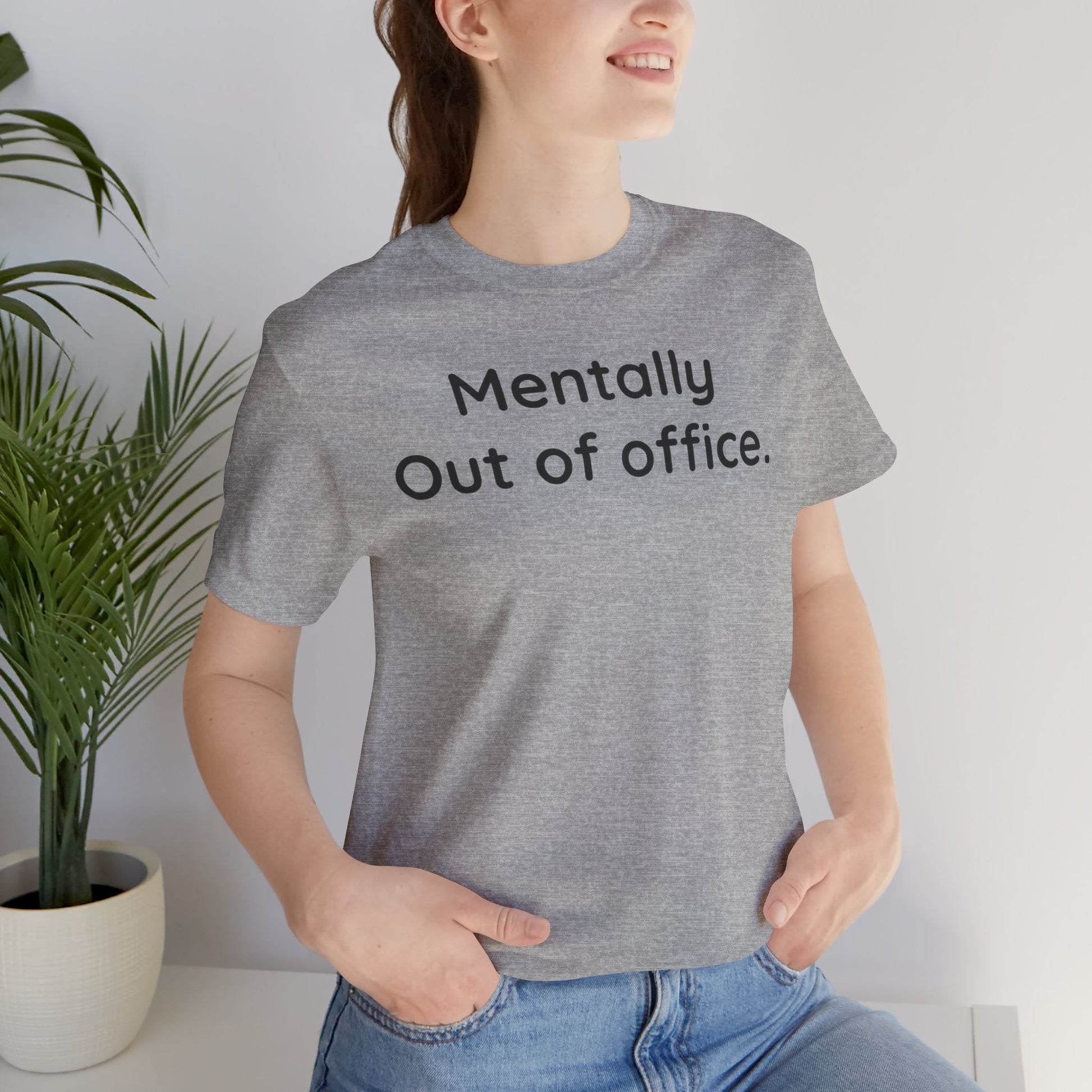 Person wearing a gray t-shirt with 'Mentally Out of Office' text, standing indoors.