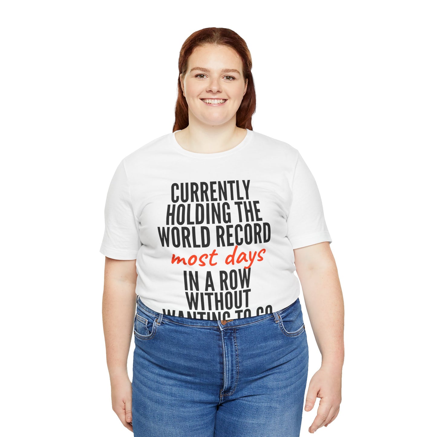 Person wearing a white t-shirt with humorous text 'Currently holding the world record most days in a row without wanting to go' design on a white background