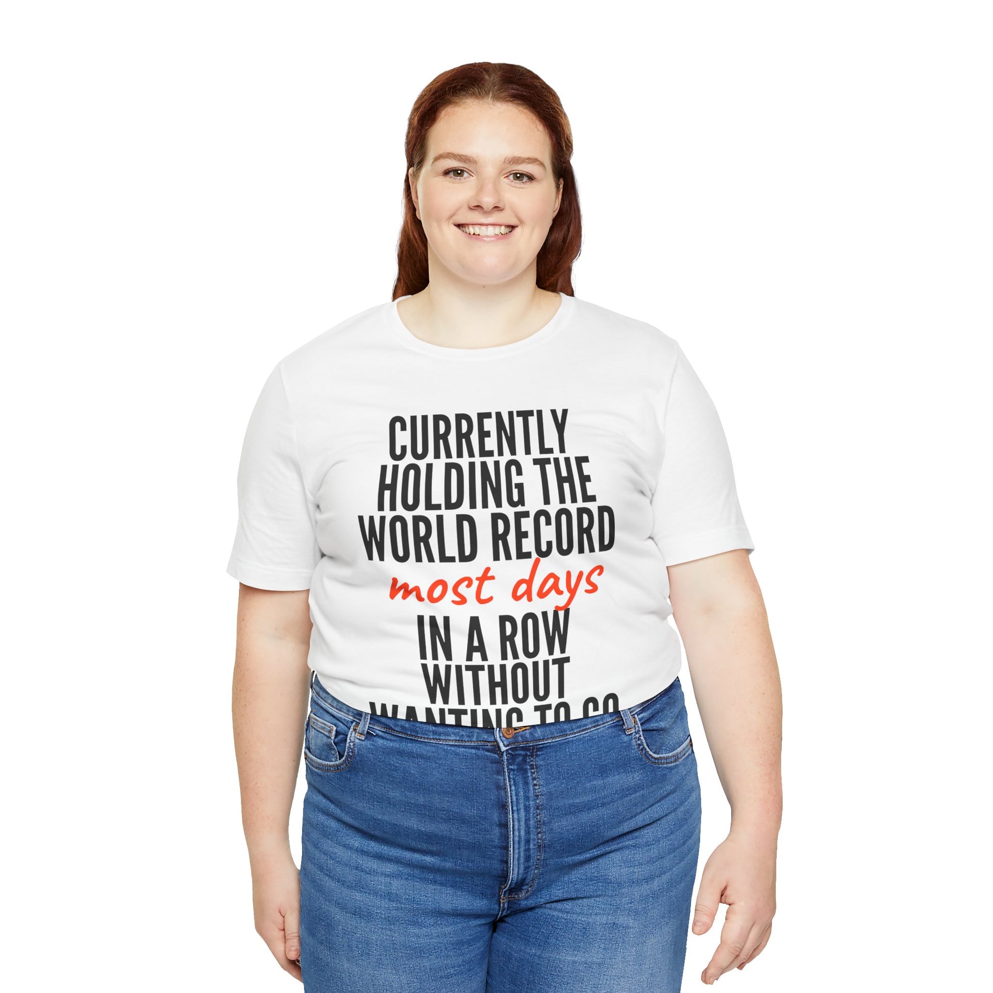 Person wearing a white t-shirt with humorous text 'Currently holding the world record most days in a row without wanting to go' design on a white background