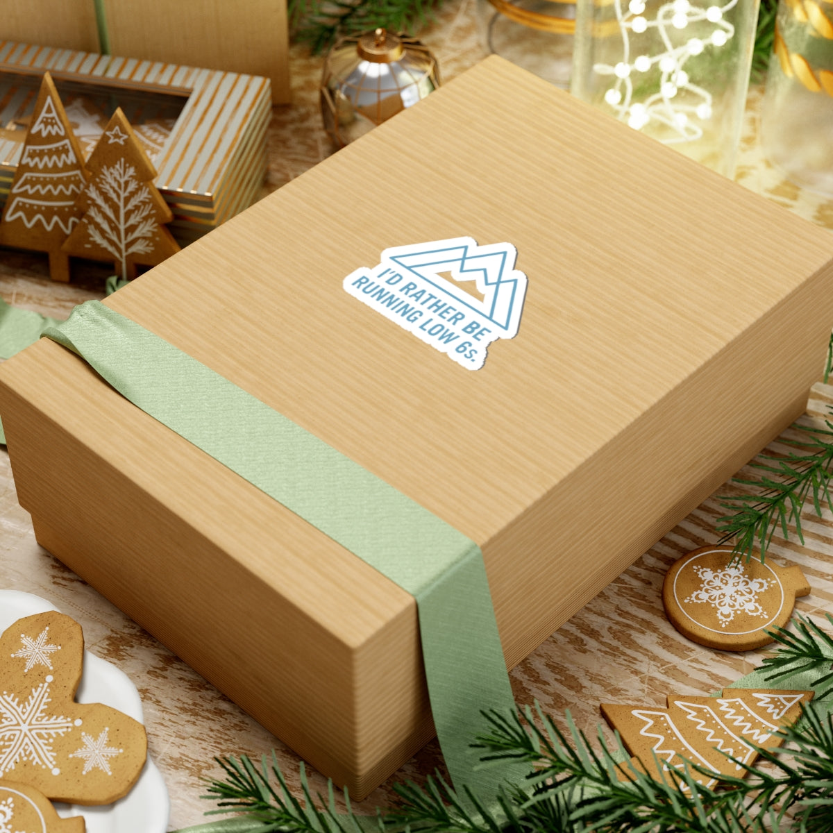 Wooden gift box with green ribbon and decorative sticker on a festive background with cookies and lights.
