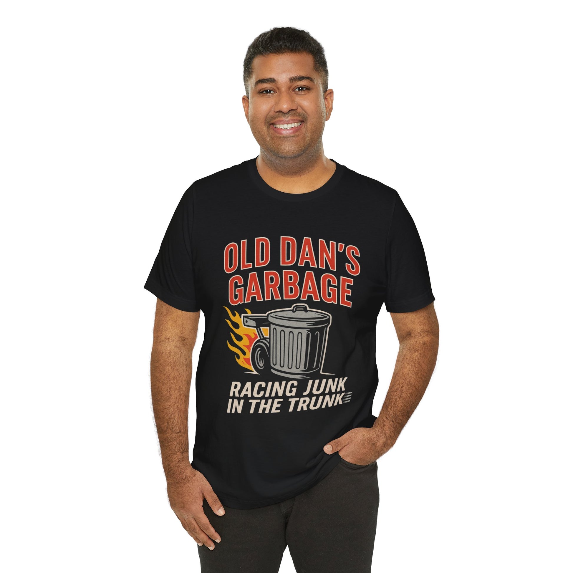 Person wearing a black graphic T‑shirt featuring the bold red and white text “Old Dan’s Garbage” above a flaming garbage can illustration, with the tagline “Racing Junk in the Trunk” below. Funny drag racing parody shirt with retro racing flames, checkered flag background, and humor‑driven hot rod style, perfect for car enthusiasts and gearhead apparel fans.