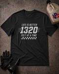 A black graphic t-shirt laid flat on a textured gray surface, featuring the white text 'LIFE IS BETTER 1320 FEET AT A TIME' with a checkered stripe design. The shirt is styled with a black glove, a funnel, and a plastic jug in a garage-themed flat lay.