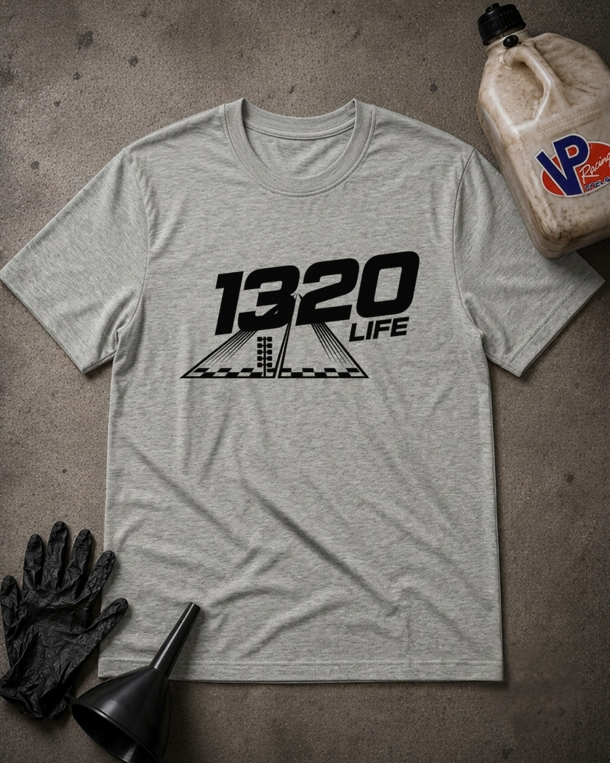 A light heather gray t-shirt with a black '1320 LIFE' graphic printed on the chest, styled in a flat-lay with black mechanic gloves, a funnel, and a plastic jug on a textured gray concrete floor.