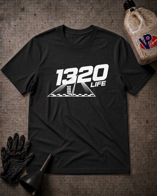 A black t-shirt with a black '1320 LIFE' graphic printed on the chest, styled in a flat-lay with black mechanic gloves, a funnel, and a plastic jug on a textured gray concrete floor.
