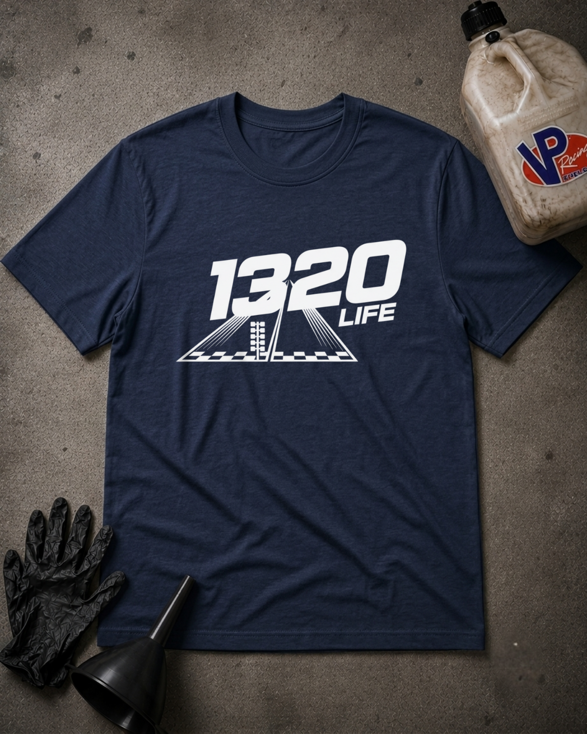 A navy  t-shirt with a black '1320 LIFE' graphic printed on the chest, styled in a flat-lay with black mechanic gloves, a funnel, and a plastic jug on a textured gray concrete floor.