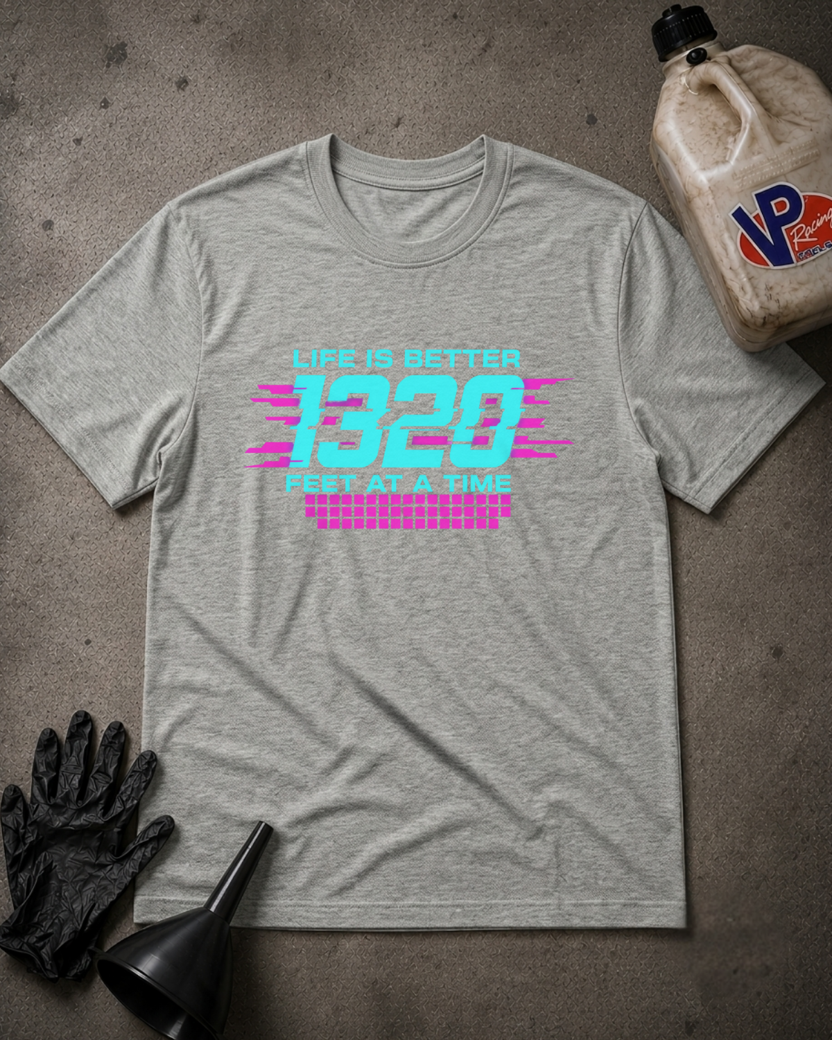 A heather gray graphic t-shirt laid flat on a textured gray surface, featuring a retro-style neon graphic that reads 'LIFE IS BETTER 1320 FEET AT A TIME' in cyan and pink. The shirt is styled with black gloves, a black funnel, and a plastic jug of VP brand oil in the corners.