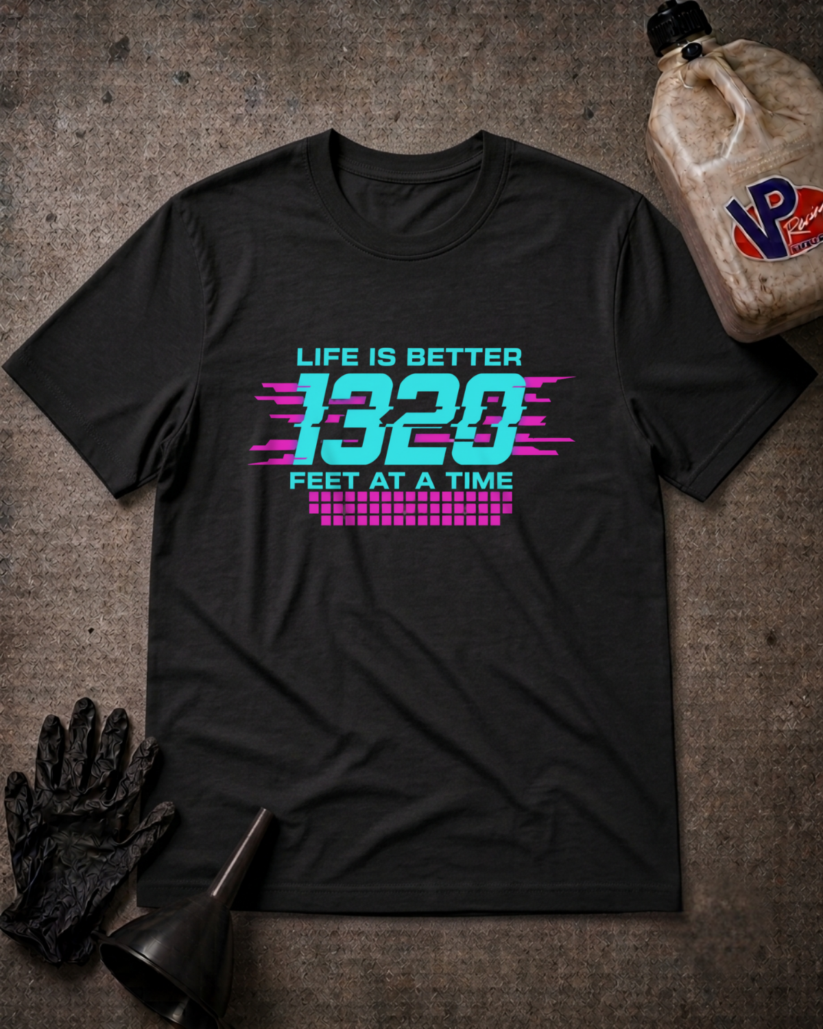 A black graphic t-shirt laid flat on a textured gray surface, featuring a retro-style neon graphic that reads 'LIFE IS BETTER 1320 FEET AT A TIME' in cyan and pink. The shirt is styled with black gloves, a black funnel, and a plastic jug of VP brand oil in the corners.