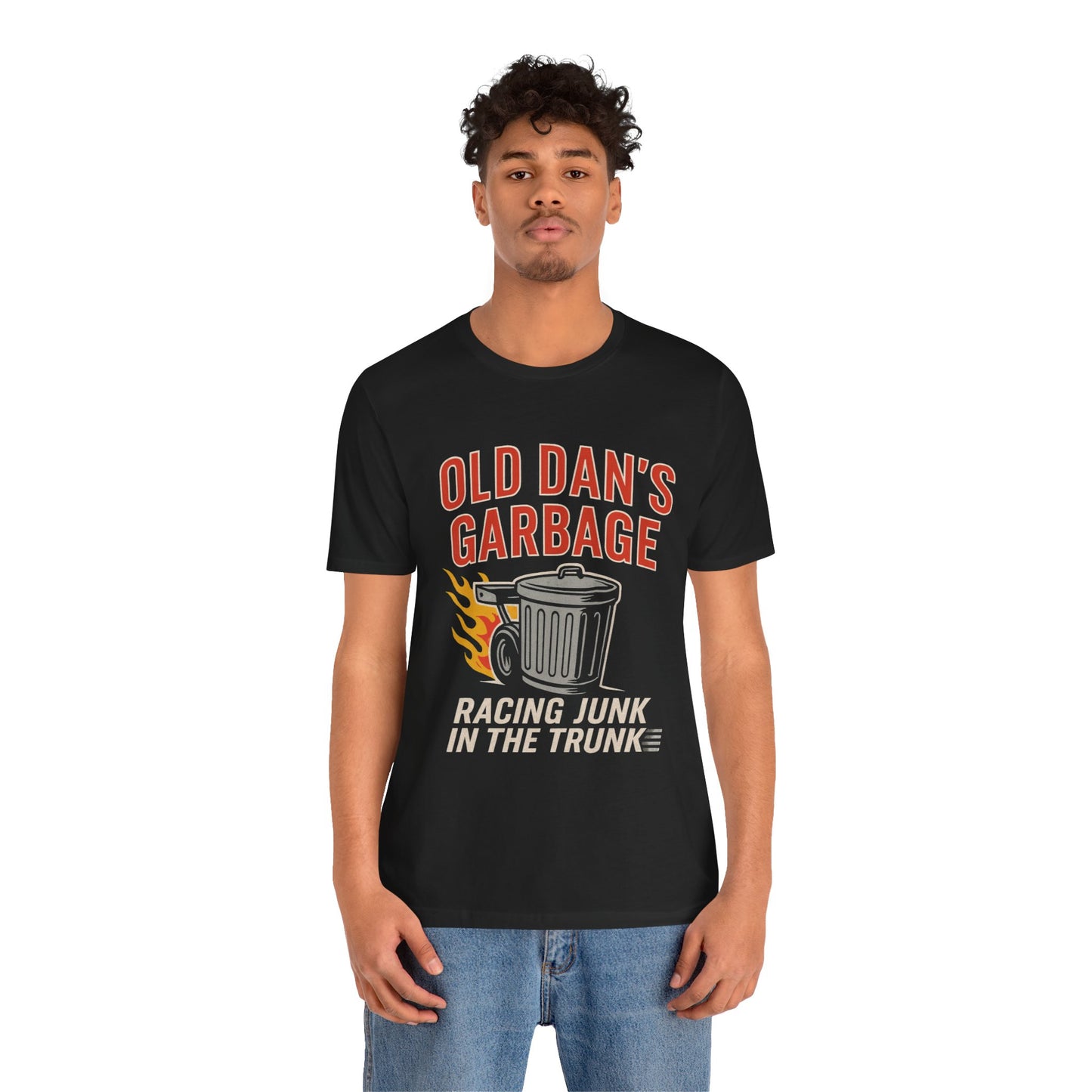 Person wearing a black graphic T‑shirt featuring the bold red and white text “Old Dan’s Garbage” above a flaming garbage can illustration, with the tagline “Racing Junk in the Trunk” below. Funny drag racing parody shirt with retro racing flames, checkered flag background, and humor‑driven hot rod style, perfect for car enthusiasts and gearhead apparel fans.