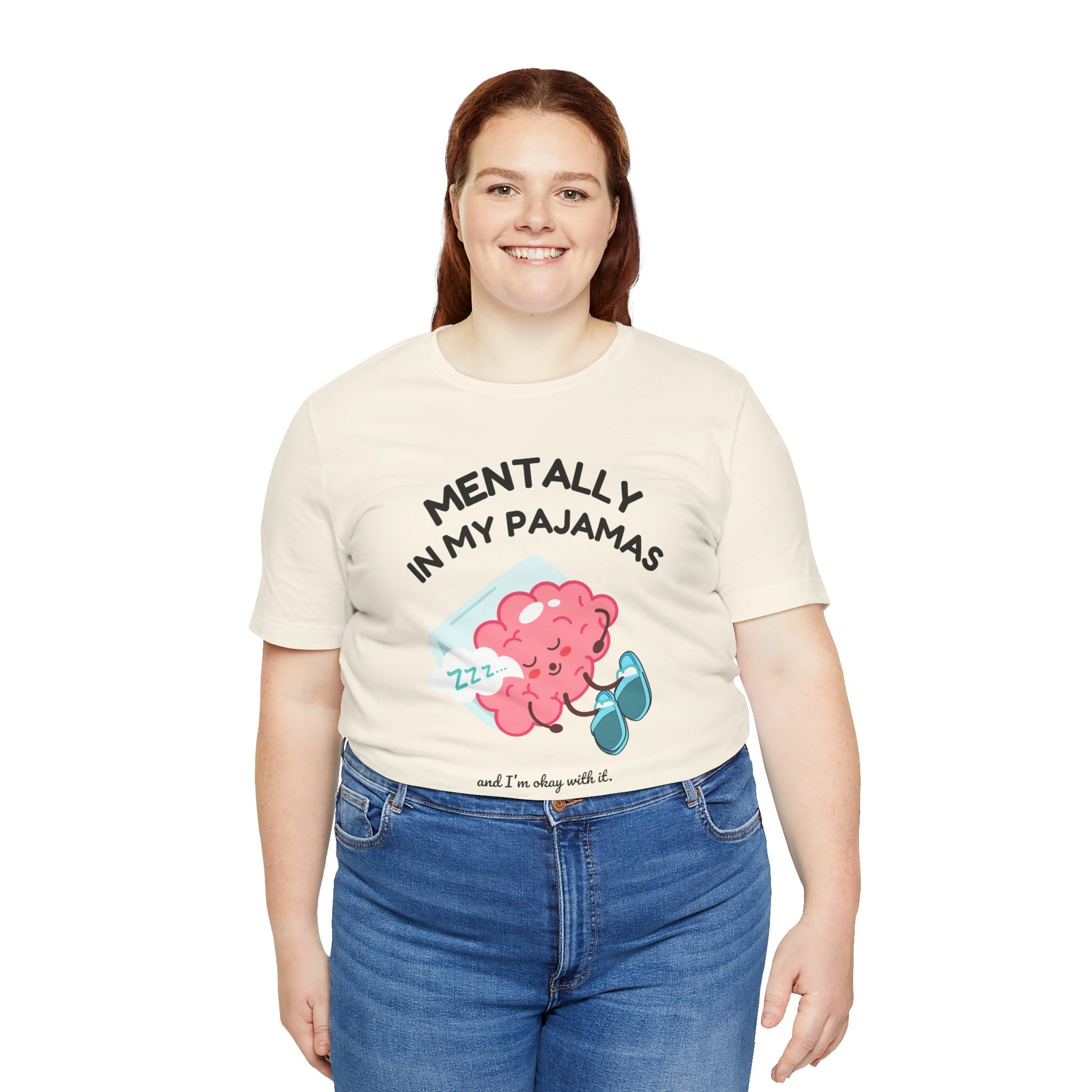 Person wearing a cream t-shirt with a graphic and text 'Mentally in my pajamas and I'm ok with it', standing against a white background
