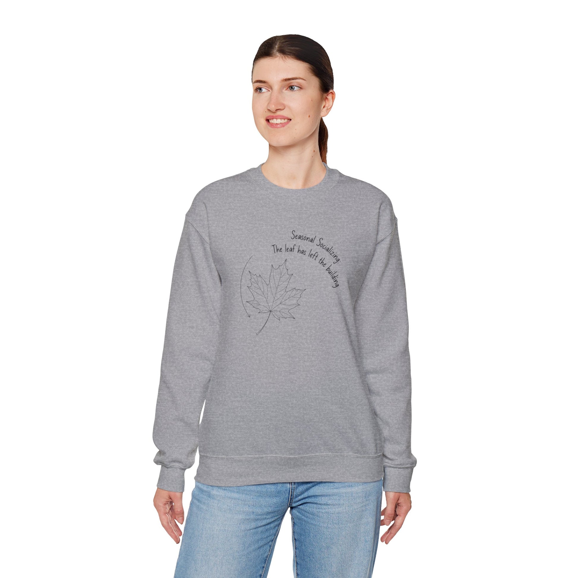 Woman wearing a gray sweatshirt with a leaf design and text 'Seasonal Socializing, The leaf has left the building' on a white background