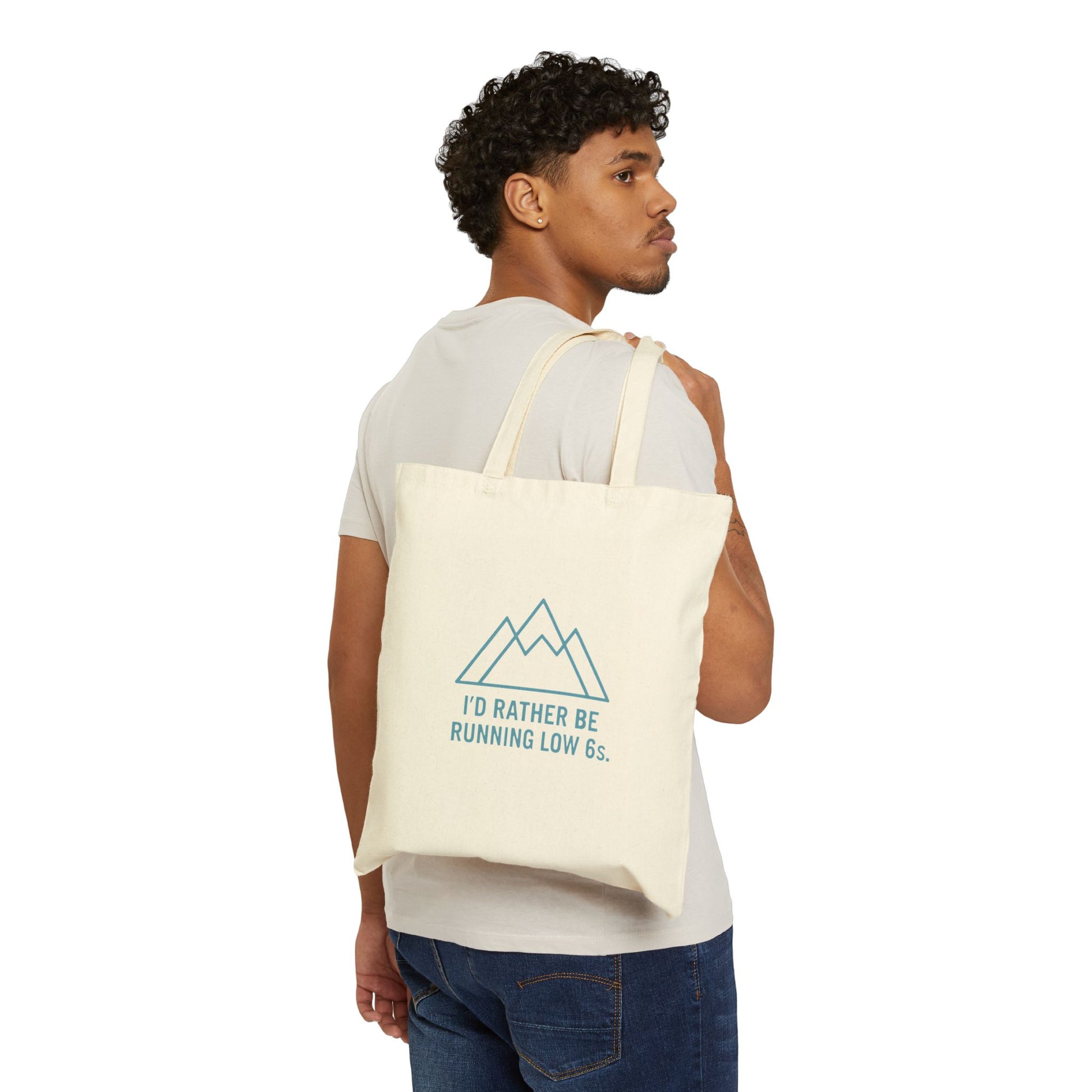 Man carrying a tote bag with a mountain design and text 'I'd rather be running low 6s' on a white background