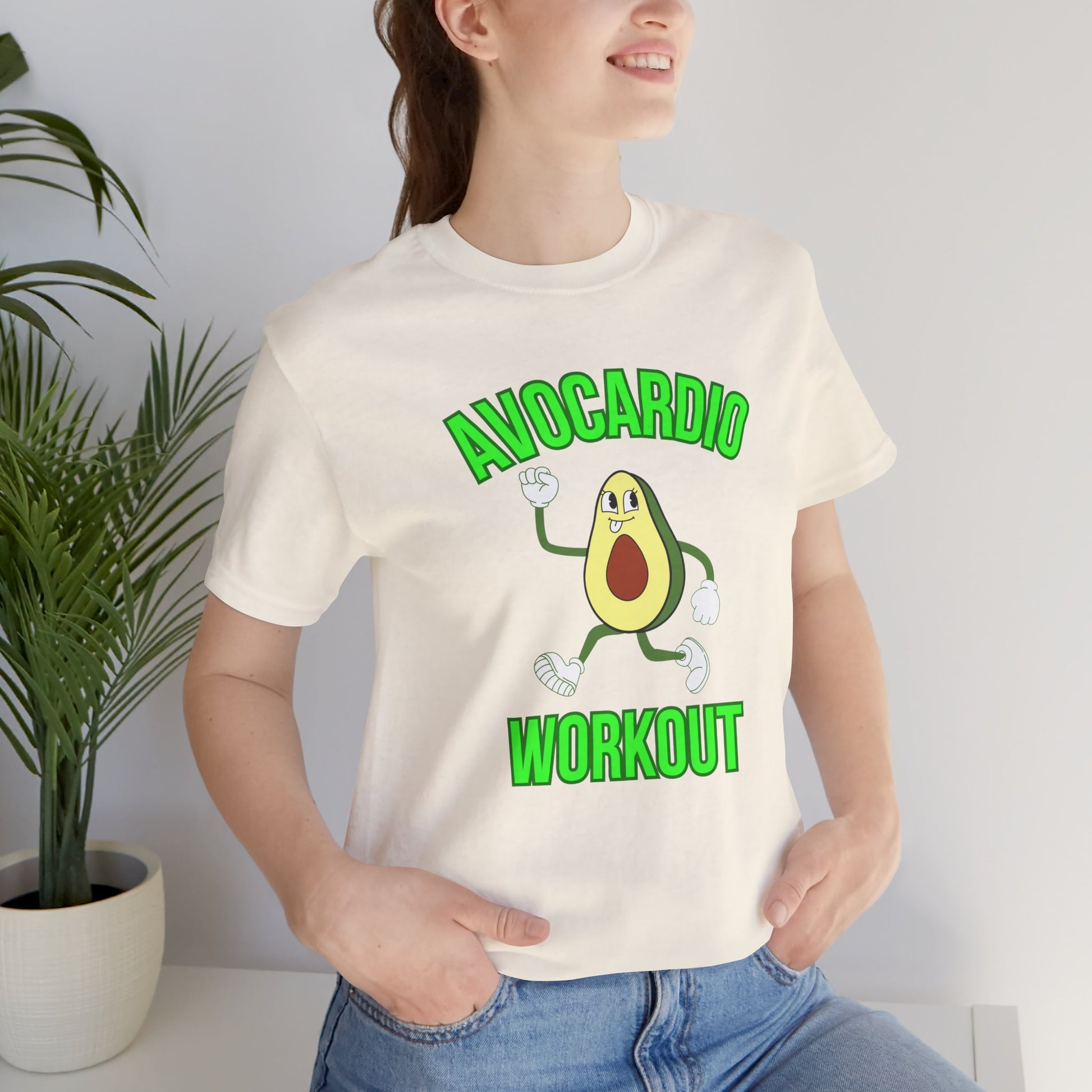 Person wearing a t-shirt with an avocado graphic and text 'Avocardio workout', standing indoors next to a plant.