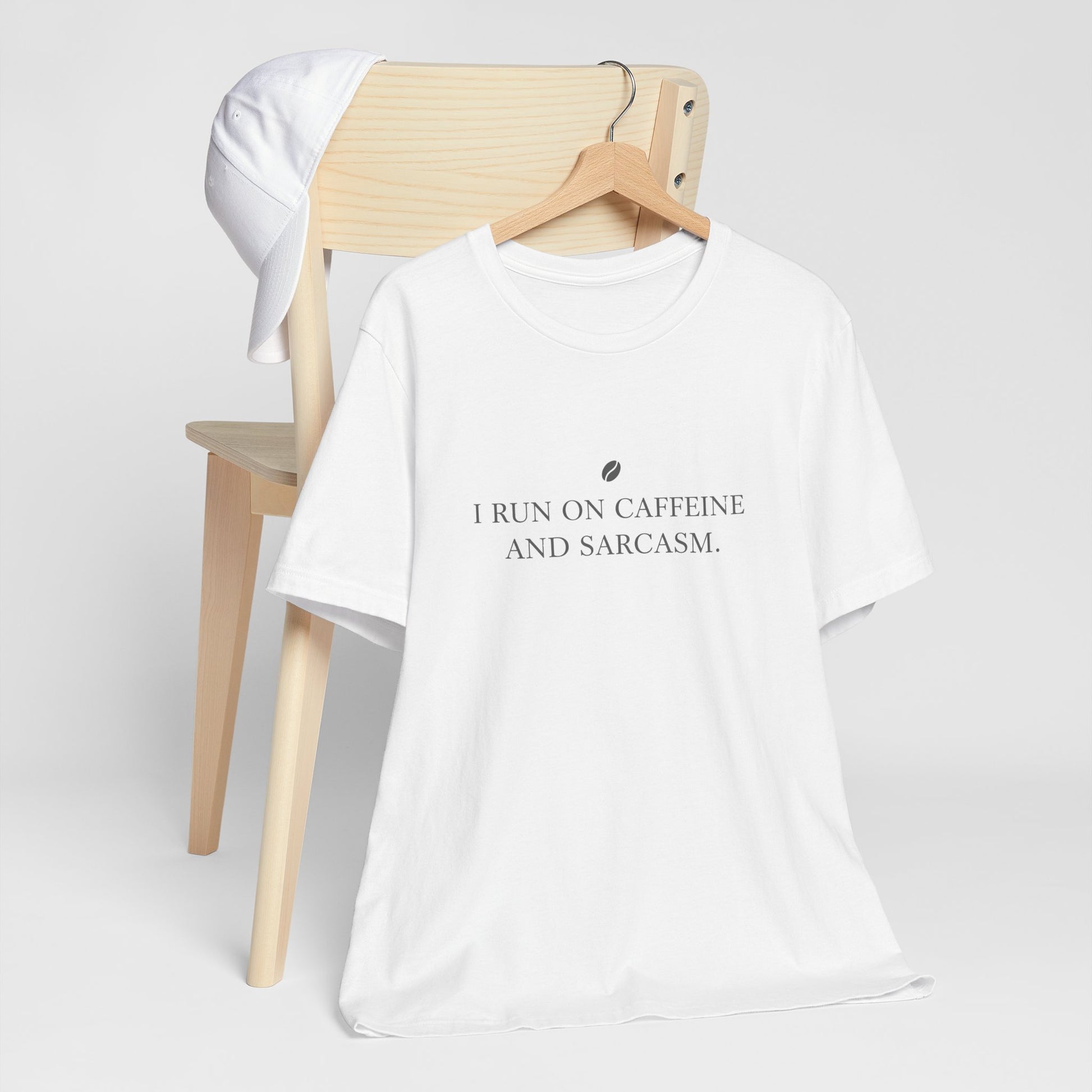 White t-shirt with text 'I run on caffeine and sarcasm' on a wooden chair against a white background